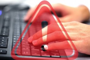 zdjęcie dłoni na klawiaturze komputera z czerwonym trójkątem z wykrzyknikiem
