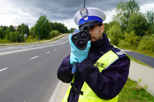 Zdjęcie przedstawia policjanta mierzącego prędkość.