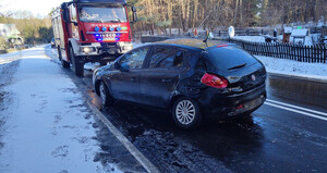 Zdjęcie przedstawia miejsce zdarzenia drogowego na DK 16 w m. Dłużki. Zdjęcie przestawia ciemne auto  stojące na drodze a obok wóz strażacki.
