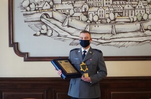 Zdjęcie przedstawia podkom. Andrzeja Łowczyka z umundurowaniu galowym na tle makiety miasta Olsztyn.