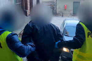 Zdjęcie przedstawia policjantów prowadzących zatrzymanego mężczyznę.