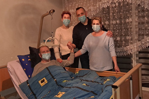 Zdjęcie przedstawia osoby na łóżkiem, w którym leży mężczyzna.