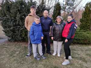 Zdjęcie przedstawia umundurowanego policjanta z grupą osób. W tel tereny zielone.