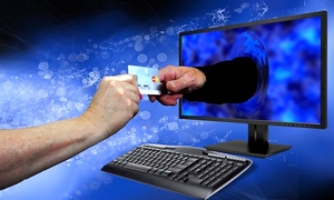 alt=&quot;dłoń trzymająca kartę kredytową i wyciągnięta druga dłoń wychodząca z ekranu komputera sięgająca po tę kartę&quot;
