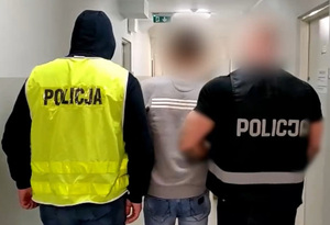 Zdjęcie przedstawia policjantów prowadzących zatrzymanego mężczyznę.