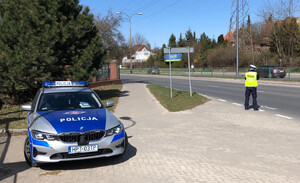 Zdjęcie przedstawia policjanta mierzącego prędkość a obok policyjny radiowóz.