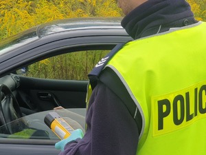 Zdjęcie przedstawia policjanta przed autem trzymającego w ręku urządzenie do badania stanu trzeźwości.