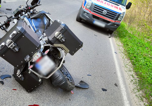 Zdjęcie przedstawia motocykl uczestniczący w zdarzeniu drogowym. A obok karetka pogotowia.