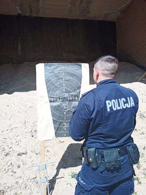 Zdjęcie przedstawia policjantów biorących udział w wyszkoleniu strzeleckim. Na zdjęciu policjant umundurowany stojący przy tarczy na której sprawdza przestrzeliny.