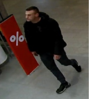 Zdjęcie przedstawia mężczyznę na terenie galerii handlowej odpowiedzialnego za dokonanie kradzieży. Mężczyzna ubrany jest w ciemnych kolorach, jest wysoki i ma ciemne włosy.