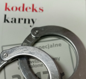 Zdjęcie przedstawia książkę z napisem kodeks karny oraz policyjne kajdanki.