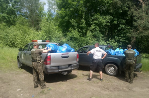 Zdjęcie przedstawia policyjnych wodniaków oraz strażników leśnych a obok pojazdy na których znajdują się zapakowane w worki śmieci.