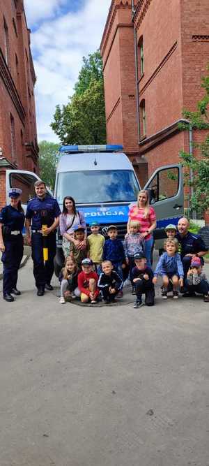 Zdjęcie przedstawia policjantów ruchu drogowego wraz z przedszkolakami i opiekunkami.