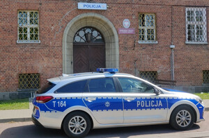Zdjęcie przedstawia radiowóz a w tle budynek Komisariatu Policji w Dobrym Mieście.