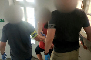 Zdjęcie przedstawia prowadzenie zatrzymanego mężczyzny.