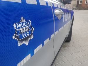 Policyjna gwiazda na drzwiach srebrnego radiowozu, na niebieskim pasku