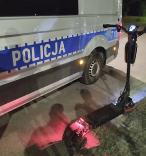 Zdjęcie przedstawia hulajnogę elektryczną a obok policyjny radiowóz.