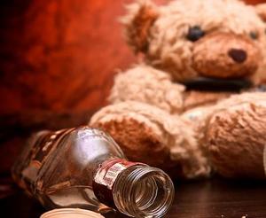 Zdjęcie przedstawia pluszowego misia oraz pustą butelkę po alkoholu.