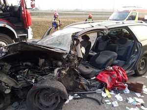 Ilustracja przedstawia miejsce wypadku drogowego. Na zdjęciu widoczne uszkodzone pojazd osobowe oraz funkcjonariusze służb ratunkowych odpowiedzialnych za bezpieczeństwo.