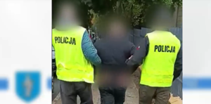Zdjęcie przedstawia kadr z nagrania podczas którego prowadzono osobę zatrzymaną w asyście dwóch policjantów.