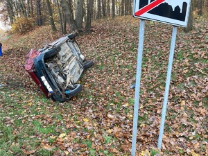 Zdjęcie przedstawia auto w kolorze czerwonym przewrócone na bok.