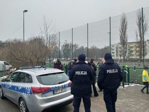 Zdjęcie przedstawia funkcjonariuszy policji i radiowóz na boisku szkolnym podczas akcji charytatywnej