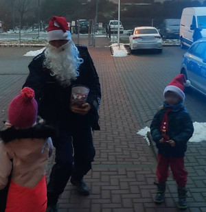 fot. st.sierż. Jarosław Nożyński Zdjęcie przedstawia funkcjonariusza w czapce Mikołaja z białą brodą, rozdającego słodycze dzieciom.