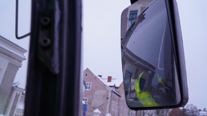 Zdjęcie przedstawia policjanta, którego wizerunek odbija się w lusterku autobusu.