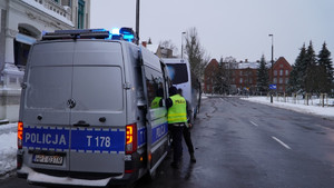 Zdjęcie przedstawia policyjny radiowóz oraz autokar i policjanta podczas kontroli.