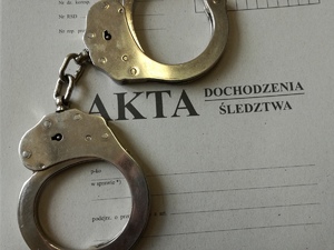 Zdjęcie przedstawia teczkę z napisem AKTA i kajdanki