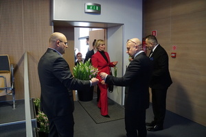 Zdjęcie przedstawia mężczyzn wręczających kobiecie kwiaty.