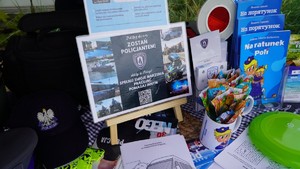 Zdjęcie przedstawia stoisko profilaktyczne - ulotki, plakat dobory do policji oraz gadżety.