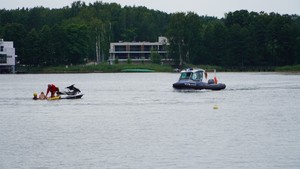 Zdjęcie przedstawia policyjną łódź oraz skuter wodny wraz z osobami na jeziorze.