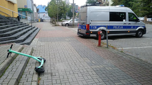 Zdjęcie przedstawia policyjny radiowóz oraz przewróconą hulajnogę na chodniku.