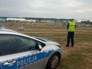 Zdjęcie przedstawia policjanta oraz radiowóz, w tle targi rolnicze.