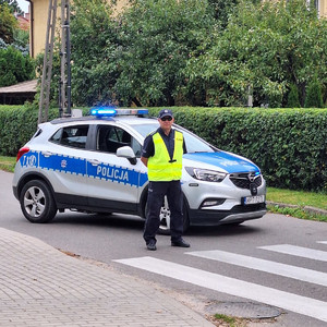 Zdjęcie przedstawia policjanta oraz radiowóz na ulicy.