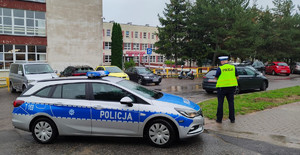 Zdjęcie przedstawia radiowóz, policjanta w pobliżu szkoły.