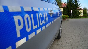 Zdjęcie przedstawia fragment radiowozu oraz w tle szkoła.