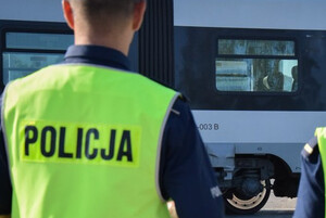Zdjęcie przedstawia fragment policjanta oraz w tle pociąg.