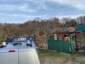 Zdjęcie przedstawia radiowóz na tle ogrodów działkowych.