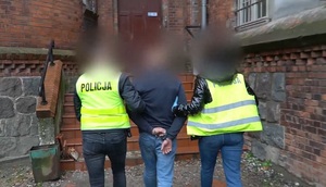 Zdjęcie przedstawia mężczyznę prowadzonego przez policjantów.