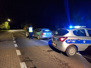 Zdjęcie przedstawia oznakowany radiowóz oraz inne auto na drodze i policjantów