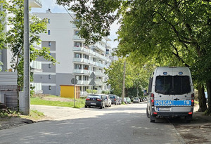 Zdjęcie przedstawia miejsce znalezienia niewybuchu oraz służby pracujące na miejscu. Na zdjęciu znajduje się policyjny radiowóz, ulica oraz blok mieszkalny.