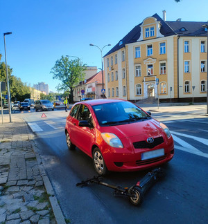 Zdjęcie przedstawia zdarzenie drogowe na al. Wojska Polskiego. Czerwone auto oraz hulajnogę elektryczną. W tle policjant ręcznie regulujący ruch.