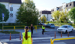 Zdjęcie przedstawia umundurowanych policjantów i ruch uliczny - pieszych oraz auta.