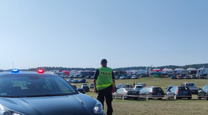 Zdjęcie przedstawia policjanta oraz auta na parkingu.