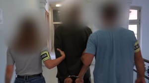Zdjęcie przedstawia prowadzenie zatrzymanego mężczyznę przez policjantów.