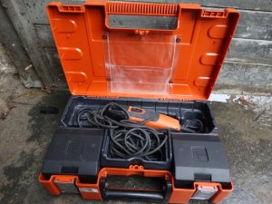 Zdjęcie przedstawia sprzęt elektrotechniczny koloru czarno-pomarańczowego w pudełku koloru czarno-pomarańczowym.